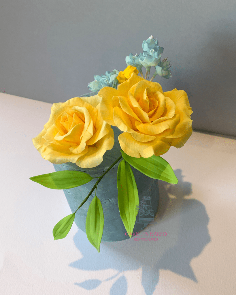4 inch cake with blue marble sugar paste. Decorated with pretty yellow sugar roses, blue filler flowers and foliage 